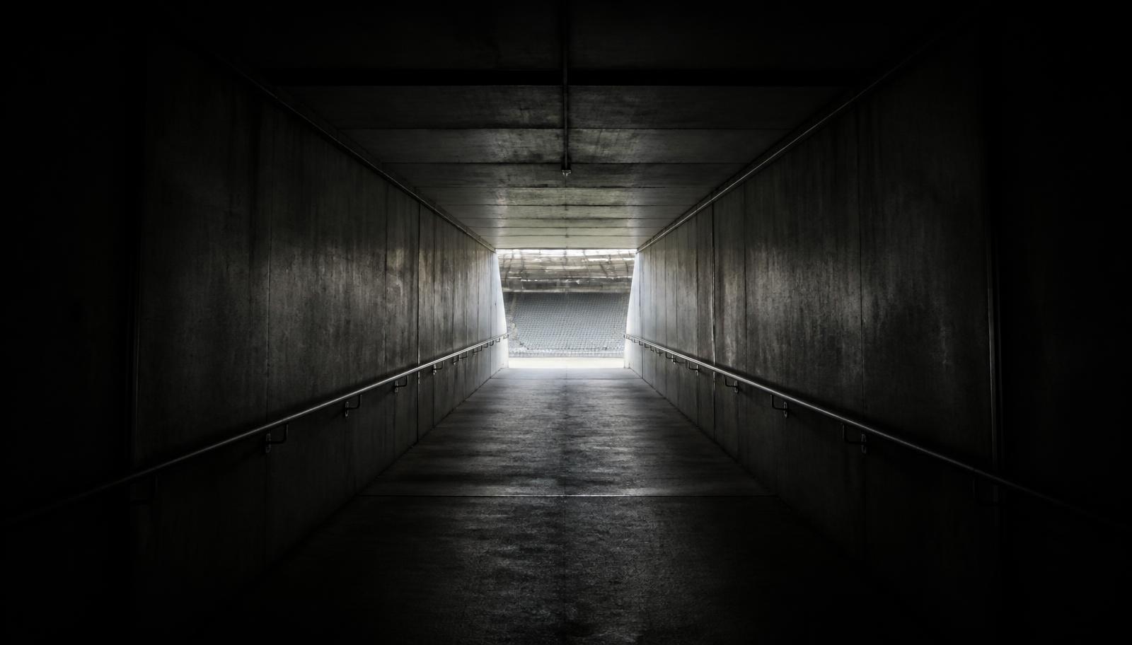 Dark concrete stadium tunnel leading to bright daylight